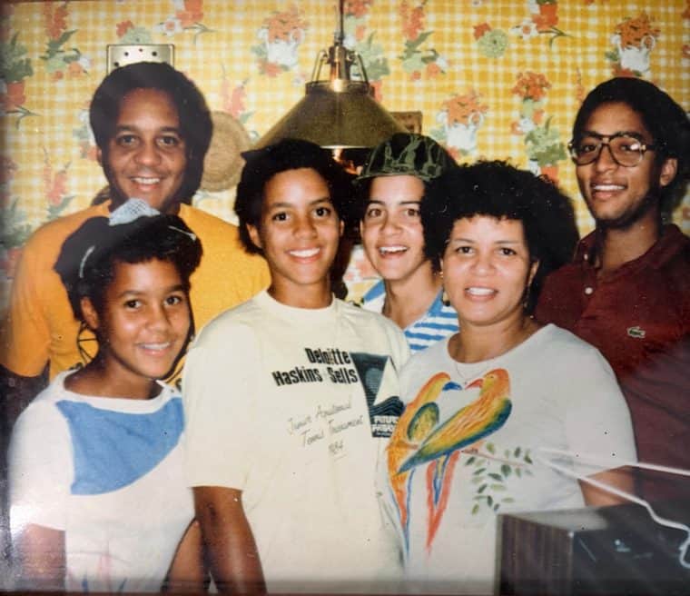 Karen in her parrot-print tee, family packed in close around her in the wallpapered kitchen, everyone beaming under the brass lamp
