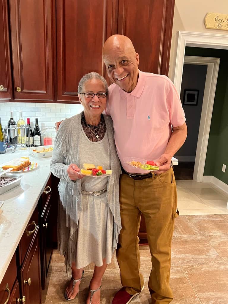 Karen arm in arm with a loved one, party plates in hand, both beaming